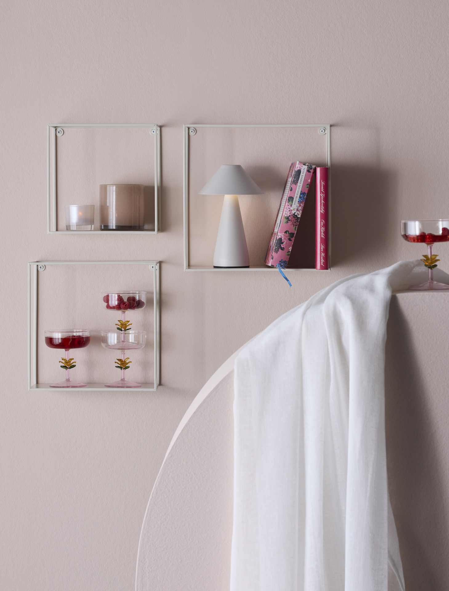 På en ljusrosa vägg hänger tre vita, moderna hyllor