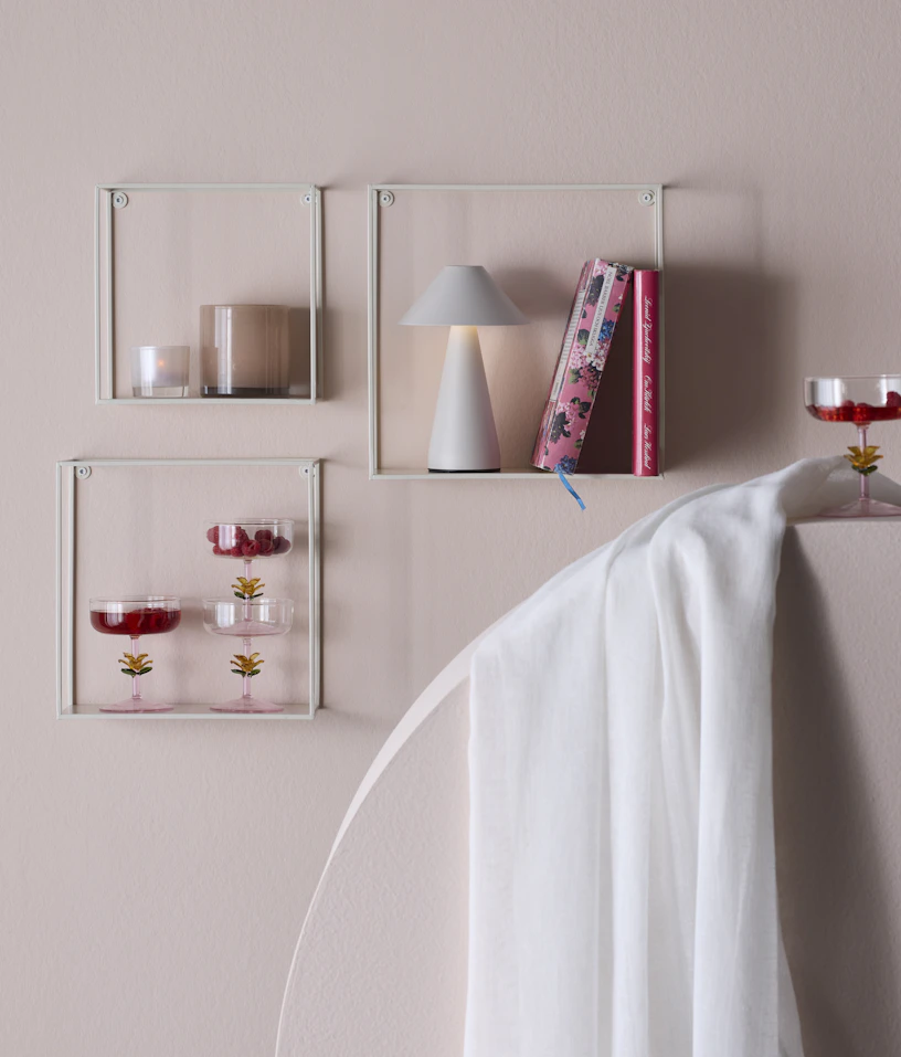På en ljusrosa vägg hänger tre vita, moderna hyllor