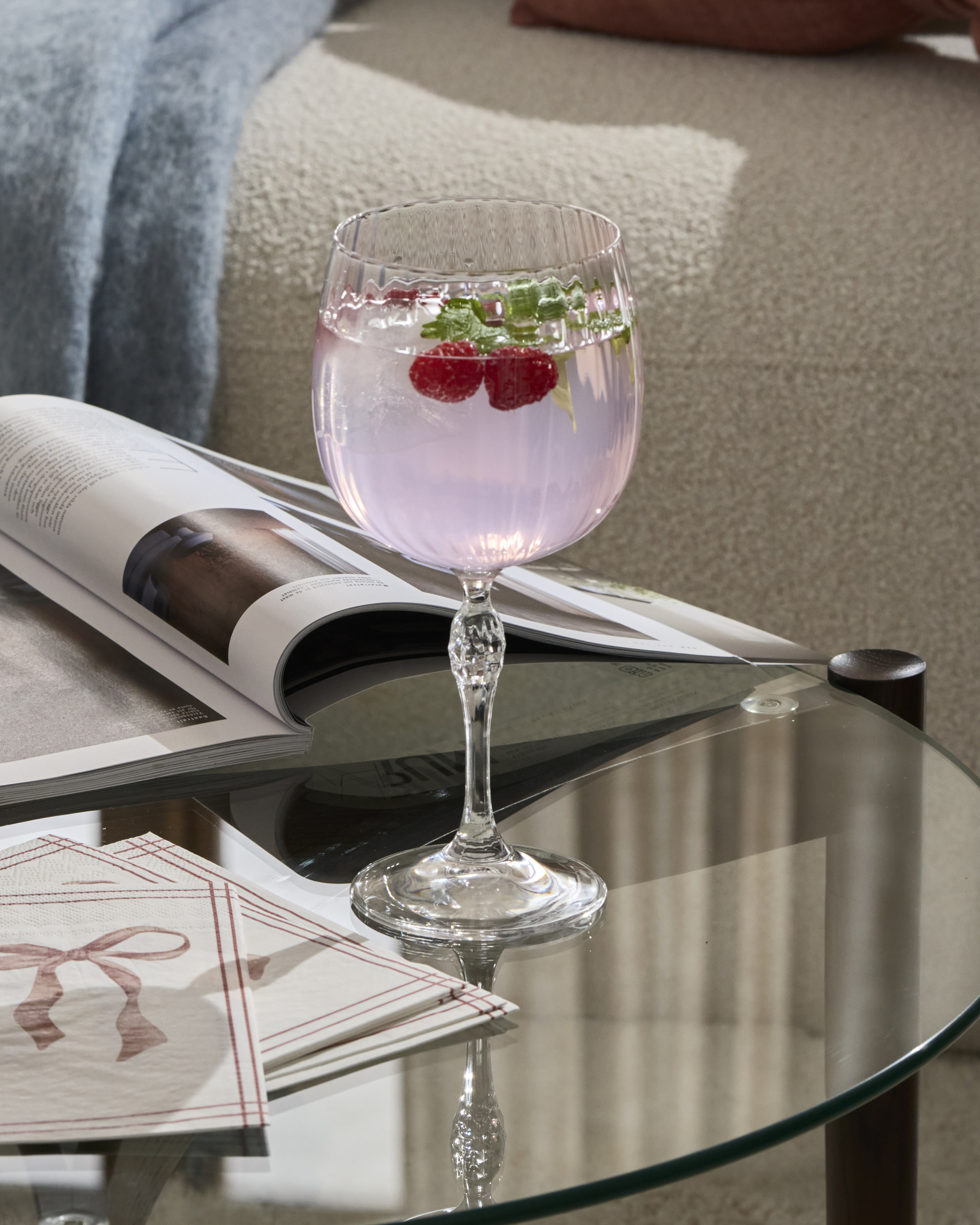 Ett drinkglas med en rosa dryck står på ett soffbord i glas