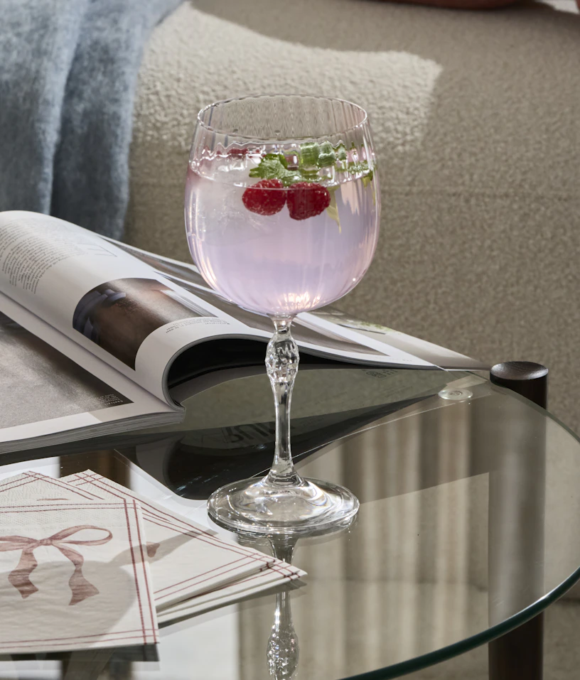 Ett drinkglas med en rosa dryck står på ett soffbord i glas