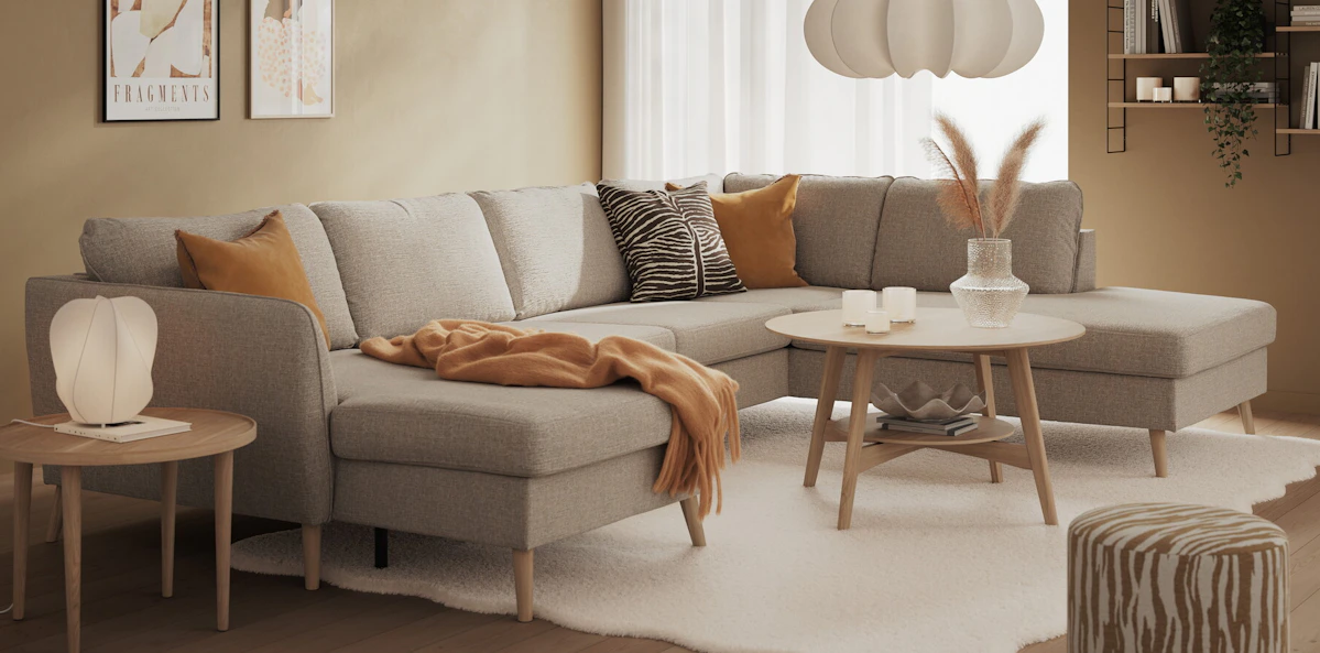 I ett beige vardagsrum står en ljusgrå, stor soffa med både schäslong och divan