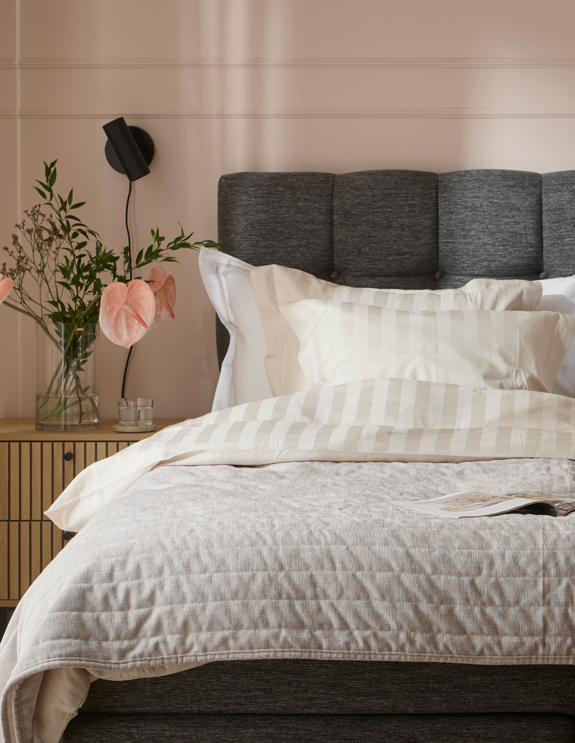 en mörkgrå säng med ljusa sängkläder framför en rosa vägg