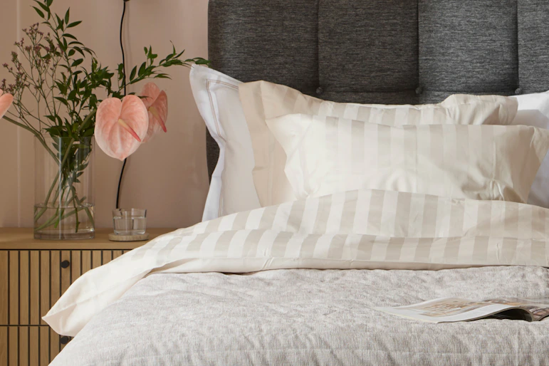 en mörkgrå säng med ljusa sängkläder framför en rosa vägg