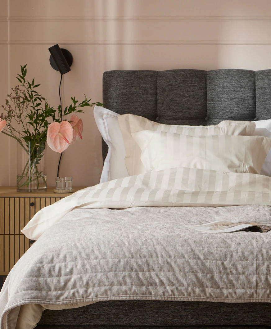 en mörkgrå säng med ljusa sängkläder framför en rosa vägg