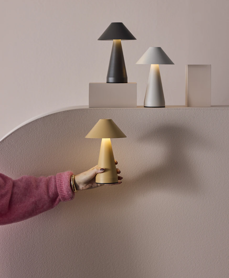 tre portabla lampor i olika färger står på ett podium framför en rosa vägg