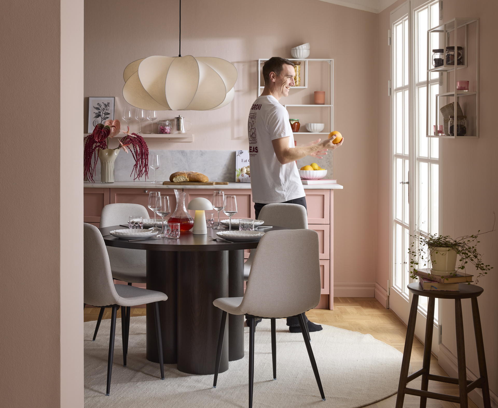 en kille går runt i ett rosa kök där det finns ett matbord med fyra gråa stolar 
