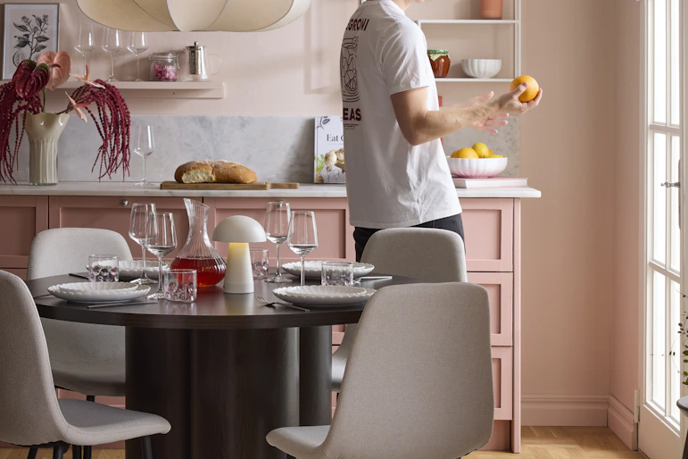 en kille går runt i ett rosa kök där det finns ett matbord med fyra gråa stolar