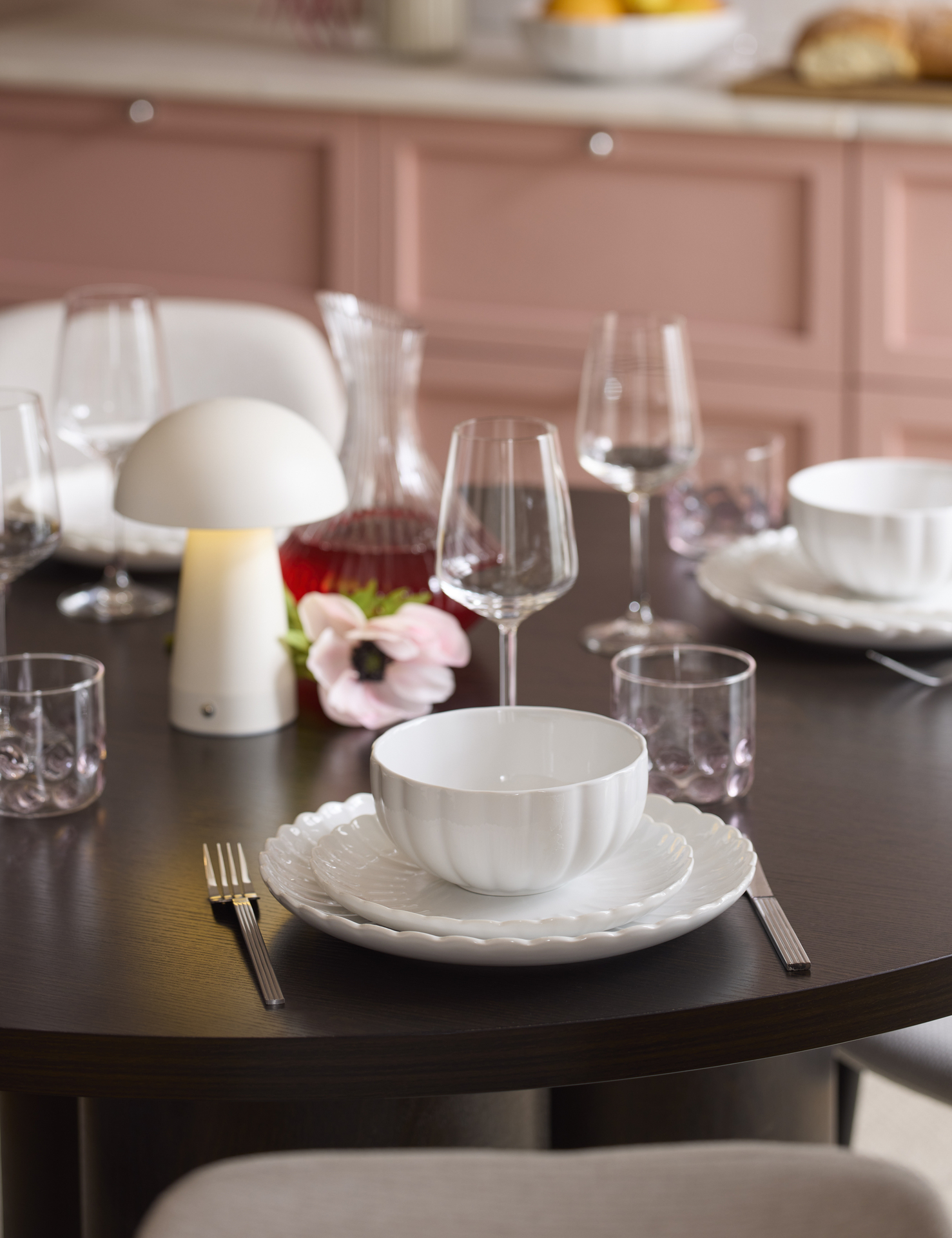 ett bord som är dukat med vitt porslin, vinglas, bestick och en vit portabel lampa