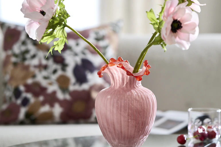 en rosa vas står på ett soffbord med rosa blommor inuti