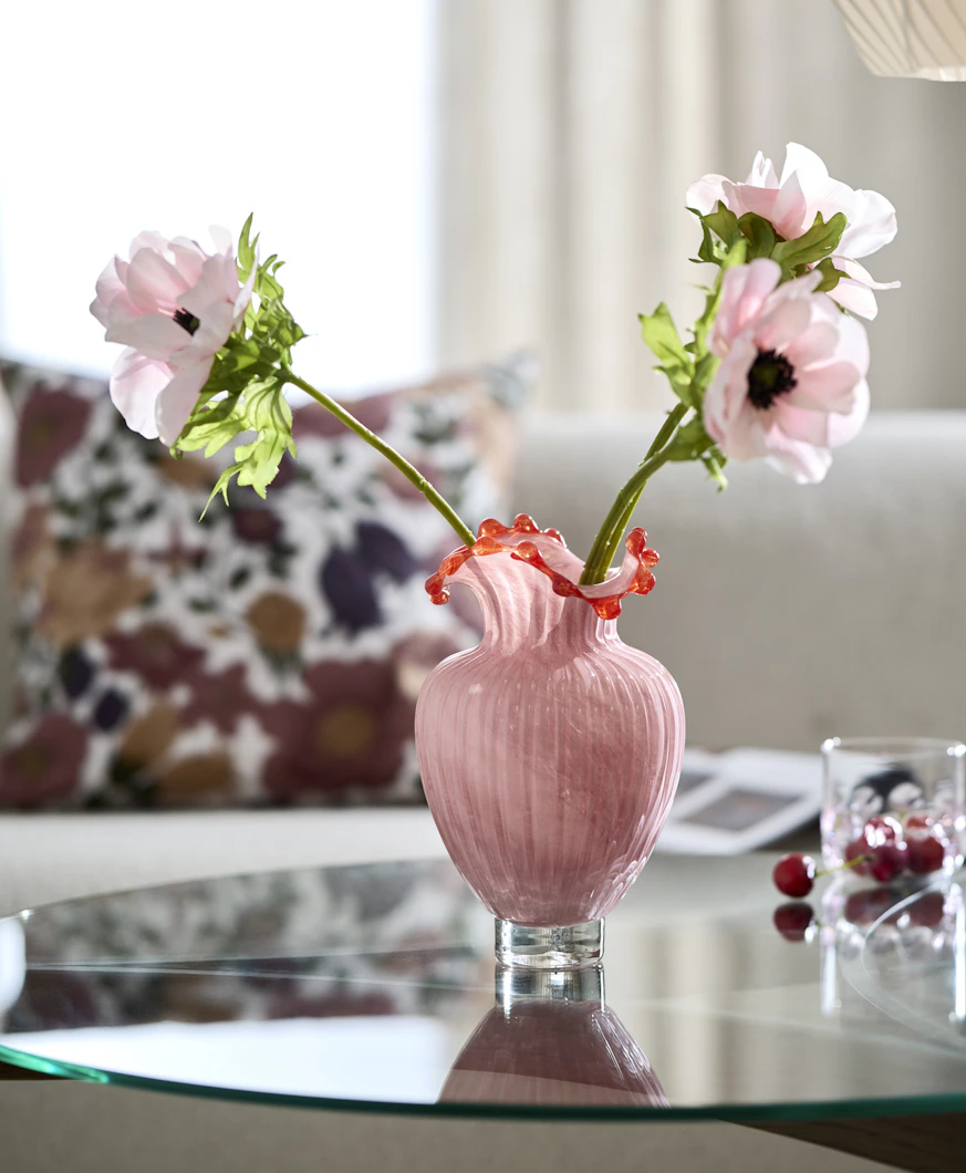 en rosa vas står på ett soffbord med rosa blommor inuti