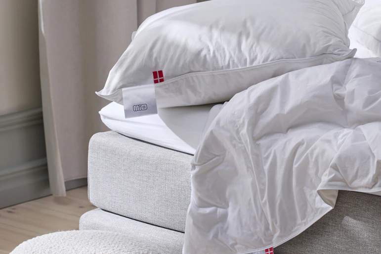 kuddar och täcken ligger på kanten av en grå säng