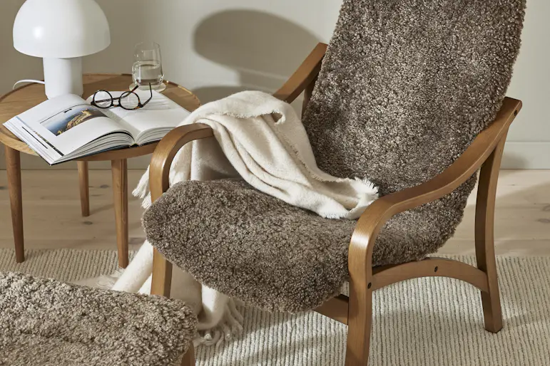 En brun fåtölj i trä med en sits i fårskinn