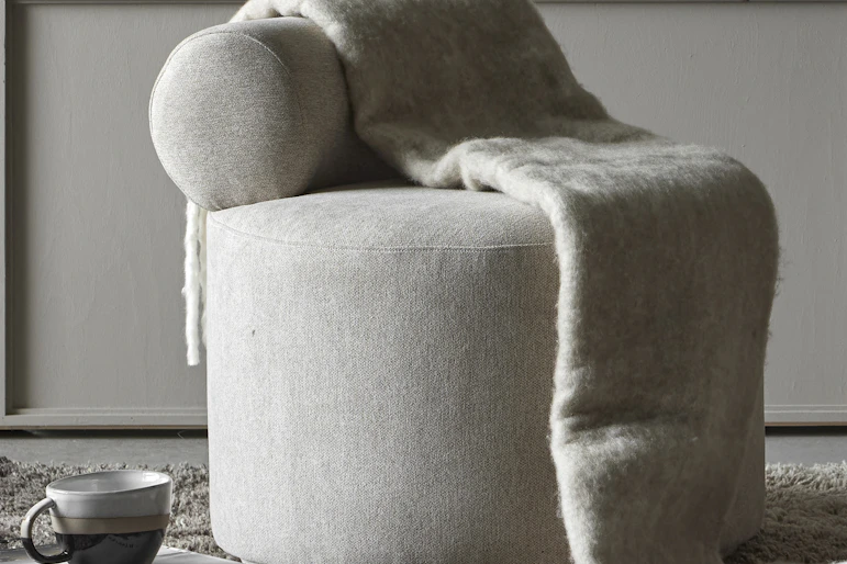 en grå puff står i ett grått rum med en grå filt