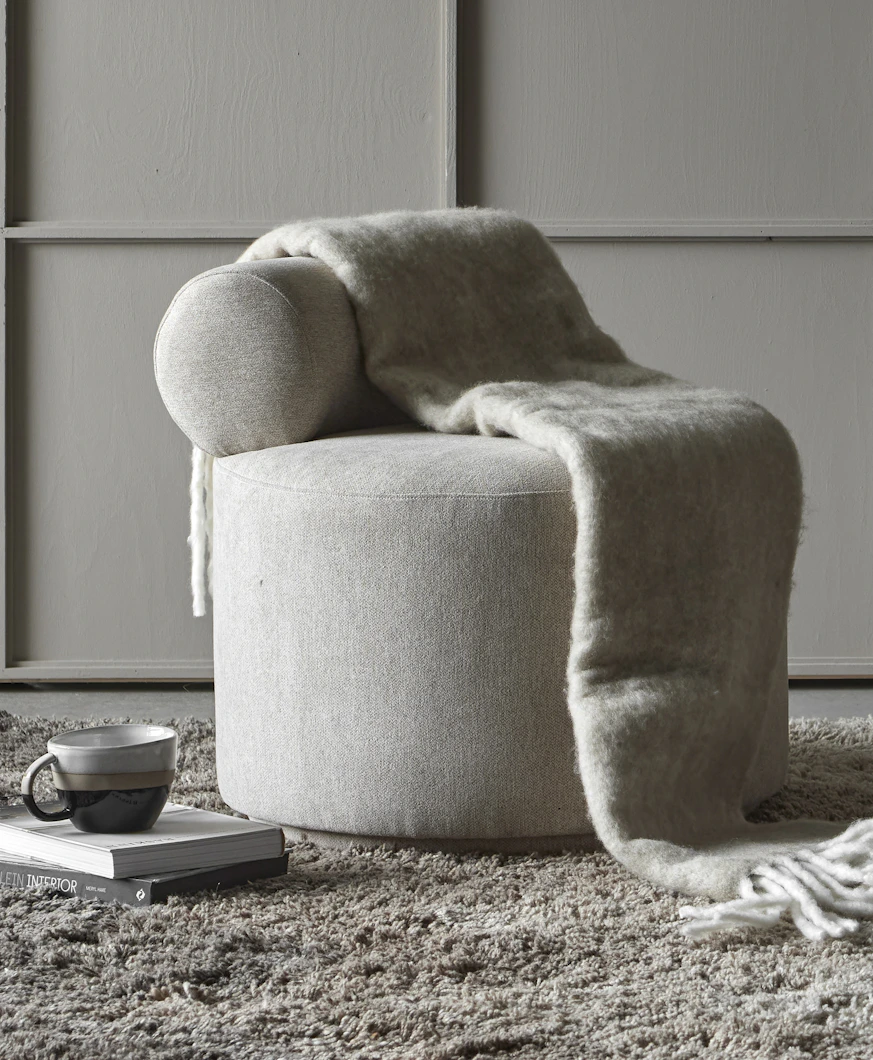 en grå puff står i ett grått rum med en grå filt