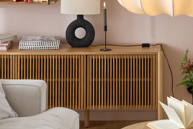 en ekfärgad tv-bänk med ribbor som luckor står framför en ljusrosa vägg