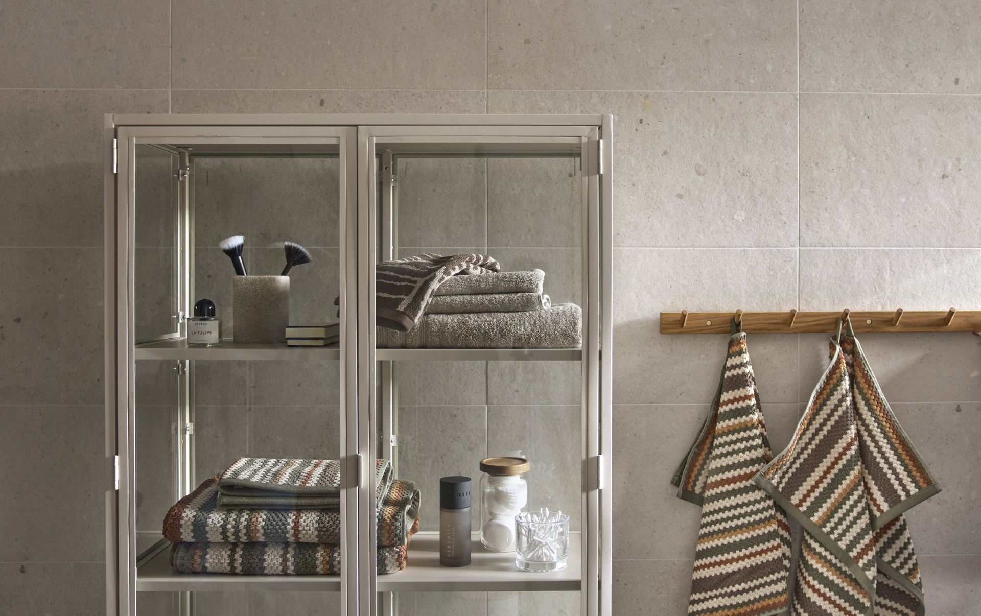 ett grått vitrinskåp i metall står i ett badrum och är fyllt av handdukar och andra badrumsartiklar