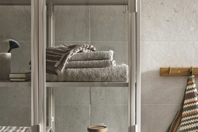 ett grått vitrinskåp i metall står i ett badrum och är fyllt av handdukar och andra badrumsartiklar