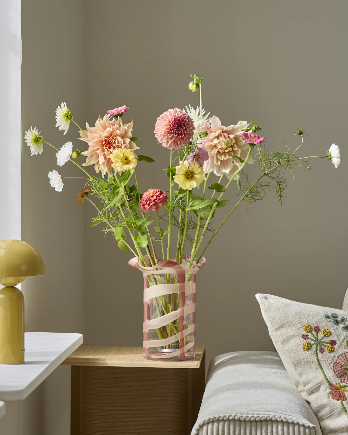 En färgglad blombukett står i en glasvas med rosa mönster.