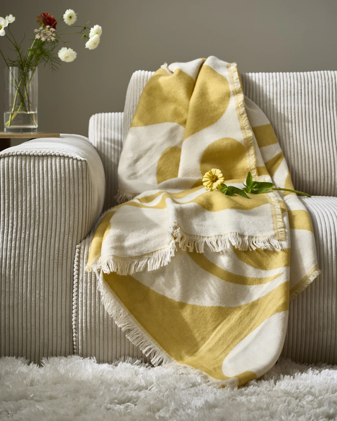 En gulmönstrad pläd ligger på en ljusgrå soffa.