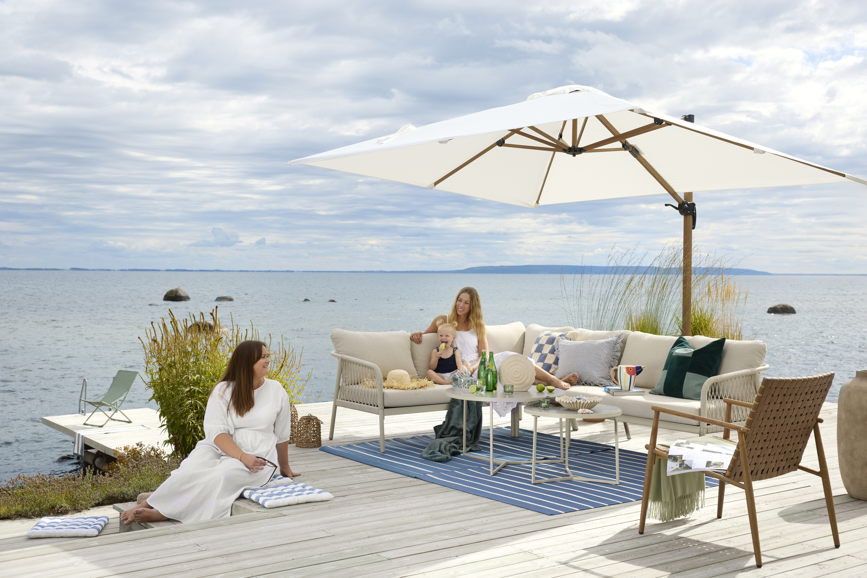 I en stor, beige utesoffa vid vattnet sitter två kvinnor och ett barn
