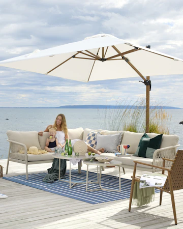 I en stor, beige utesoffa vid vattnet sitter två kvinnor och ett barn