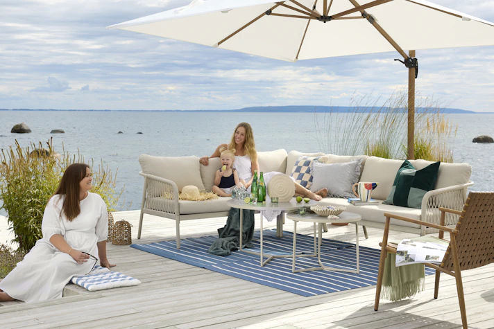 I en stor, beige utesoffa vid vattnet sitter två kvinnor och ett barn