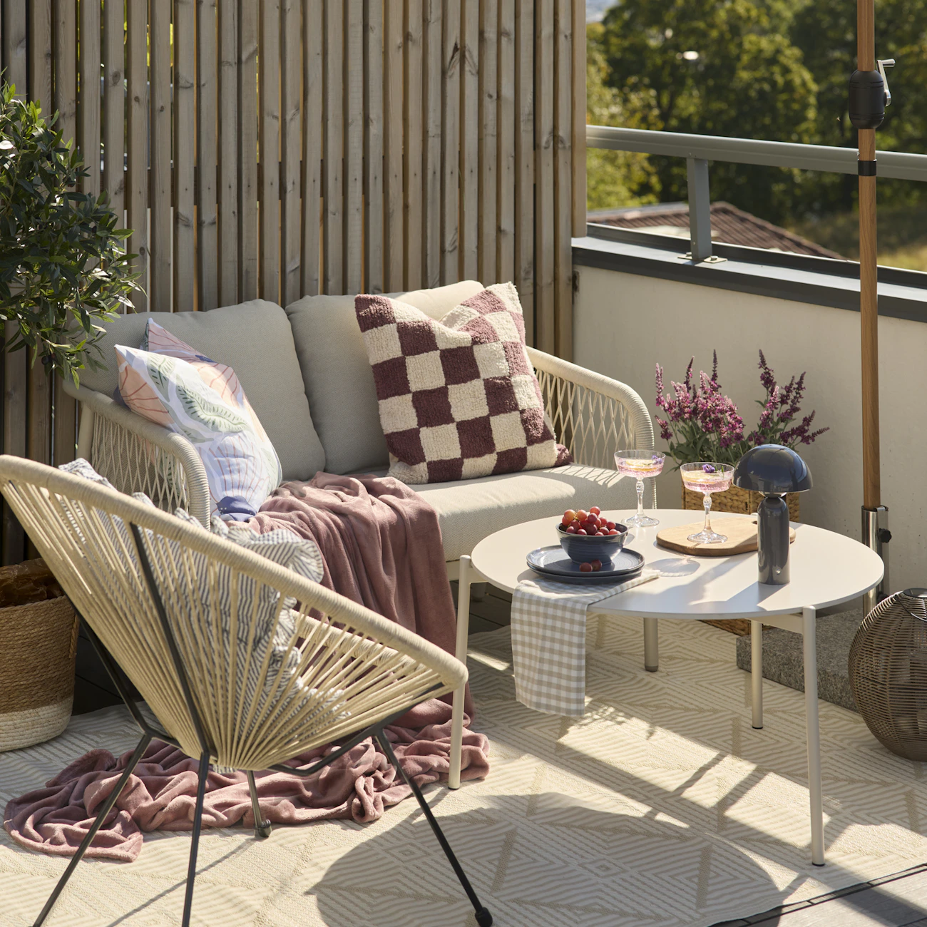 På en balkong står en beige utesoffa, en fåtölj och ett bord