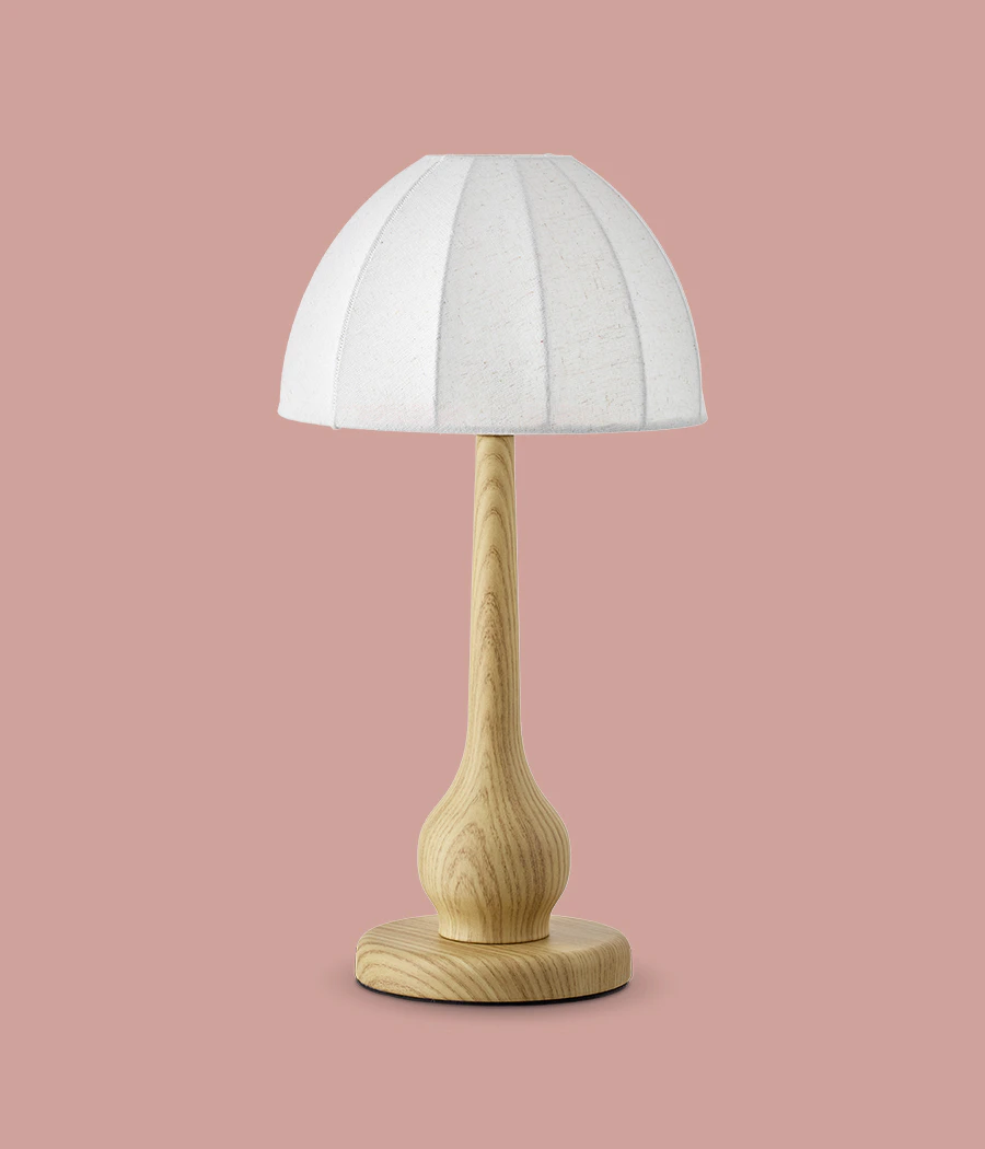 En lampfot i ljust trä med vit skärm är frilagd på en rosa bakgrund