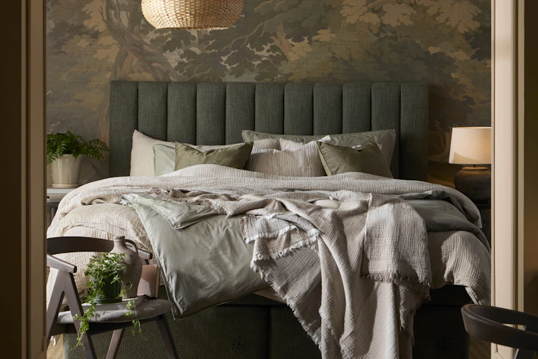 en grön kontinentalsäng står bäddad i ett mörkt sovrum