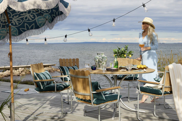 På en brygga står en kvinna intill en klassisk utegrupp i teak.