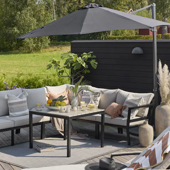 Stor utehörnsoffa med stomme av svart aluminium och gråa dynor står under ett grått parasoll på en altan.