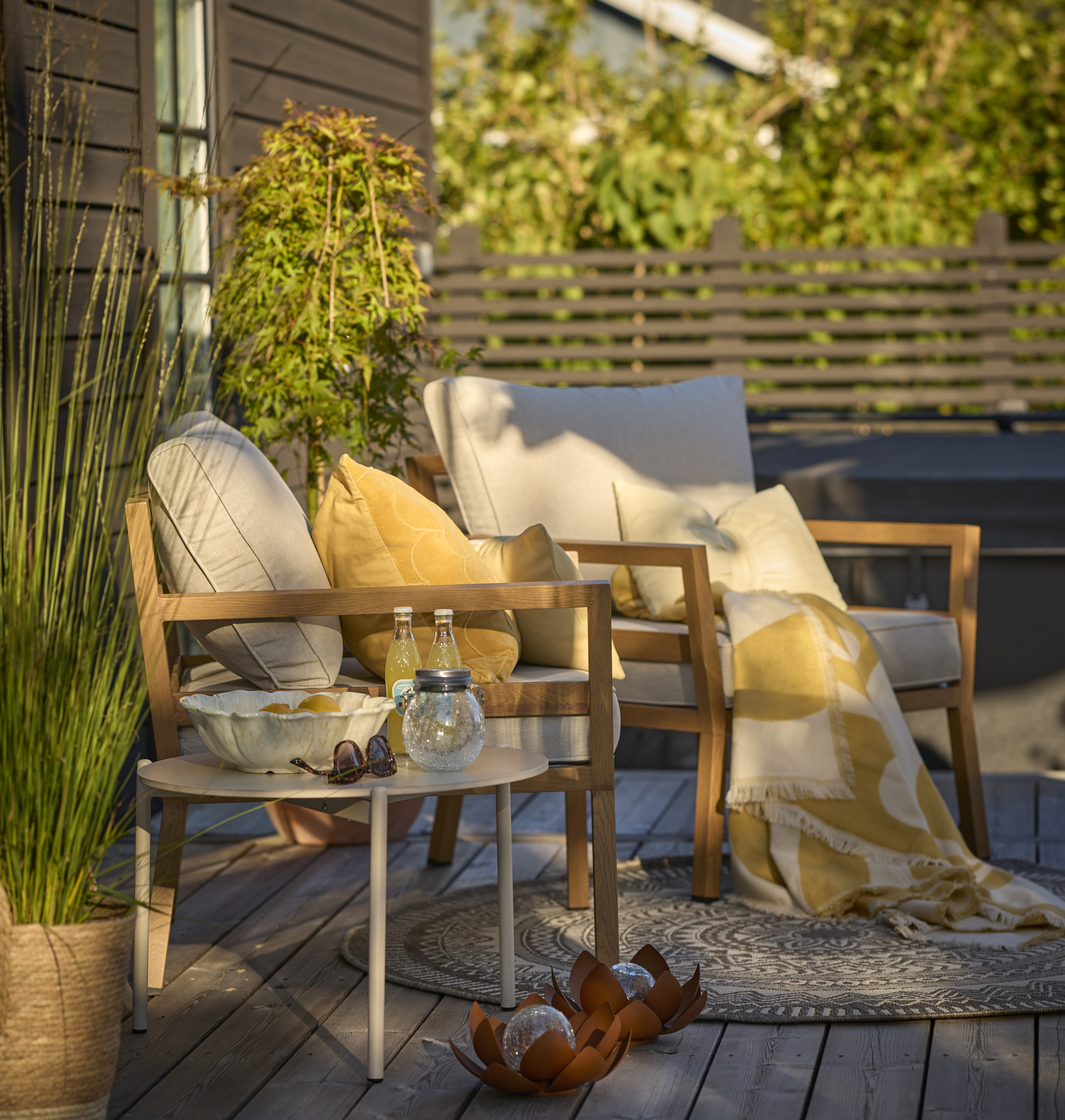 Två fåtöljer med gula kuddar och plädar står på ett trädäck.