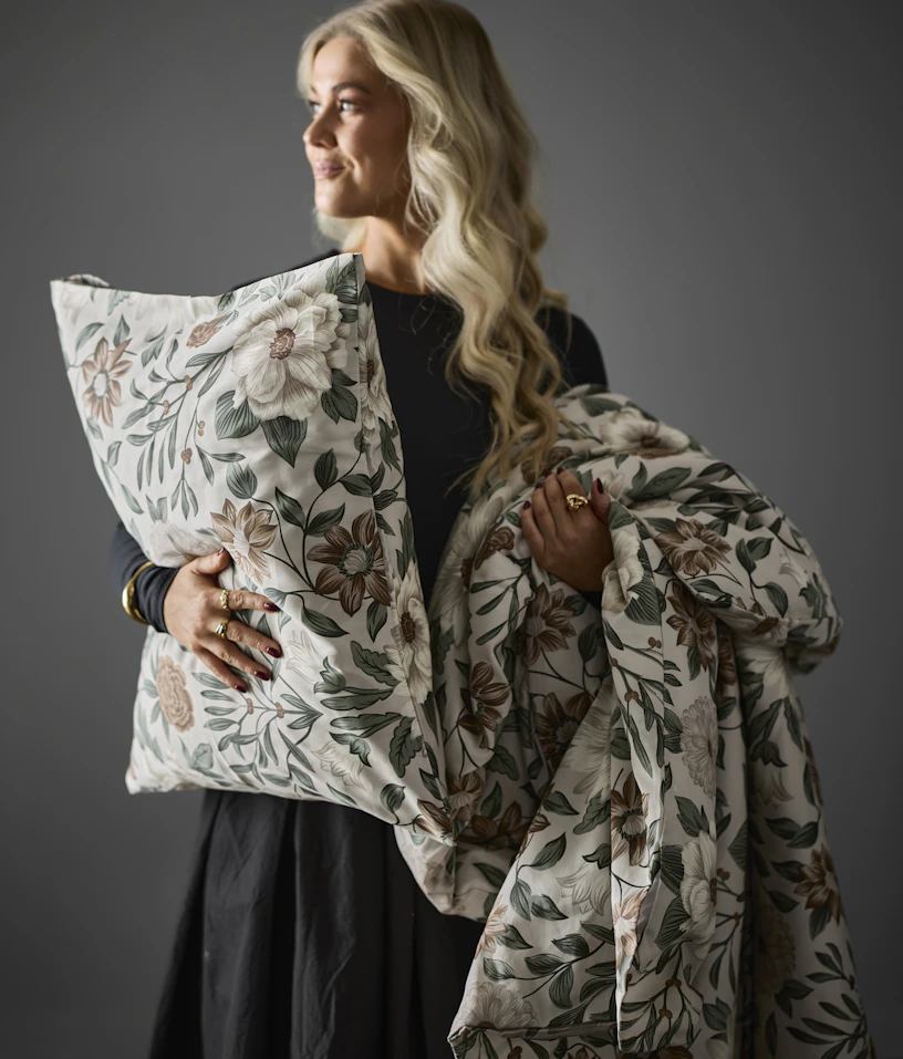 Kvinna håller upp en kudde och ett täcke med ett mönstrat påslakan