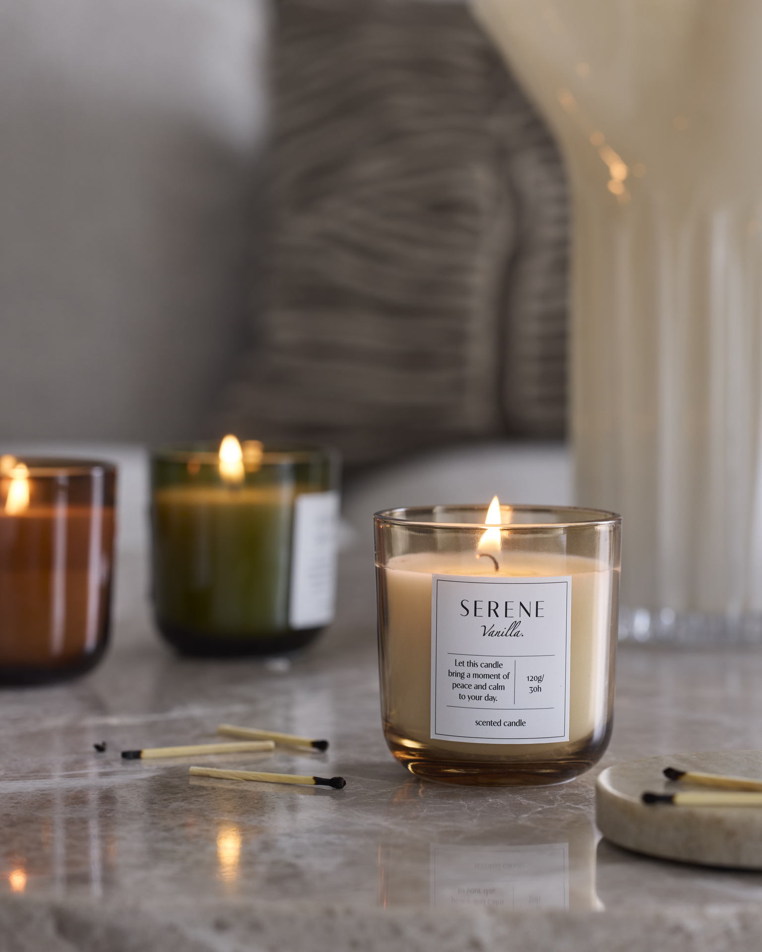 tre doftljus i olika färger är tända och står på en stenskiva, bredvid utplacerade tändstickor