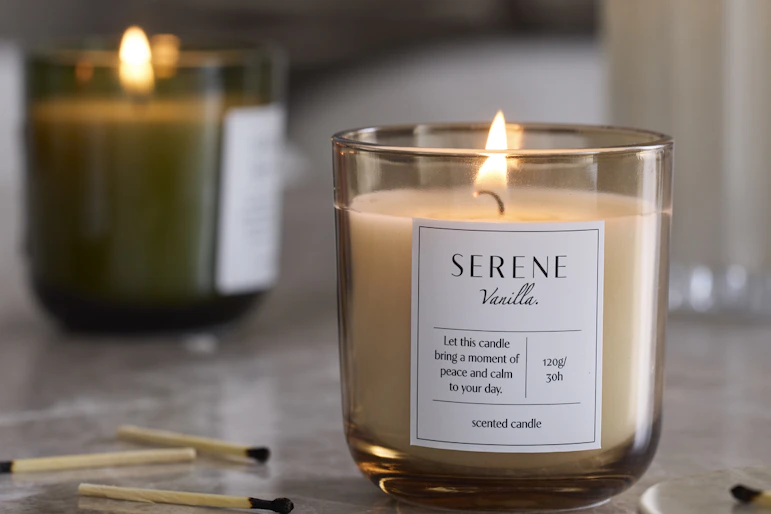 tre doftljus i olika färger är tända och står på en stenskiva, bredvid utplacerade tändstickor