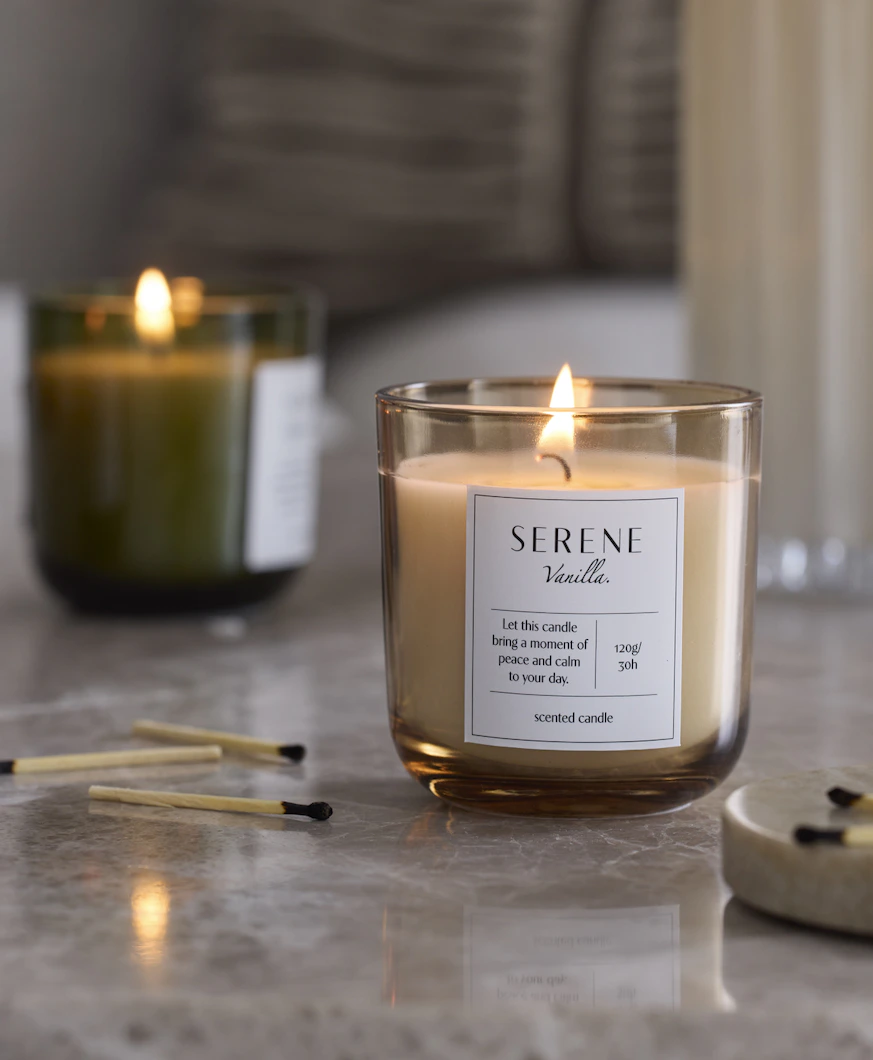 tre doftljus i olika färger är tända och står på en stenskiva, bredvid utplacerade tändstickor