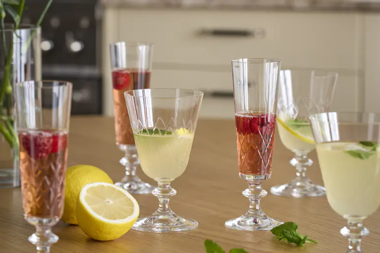 Flera glas i olika stilar fyllda med röd och gul dryck står på ett bord.