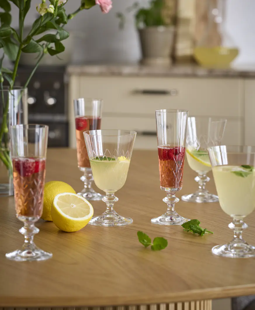 Flera glas i olika stilar fyllda med röd och gul dryck står på ett bord.