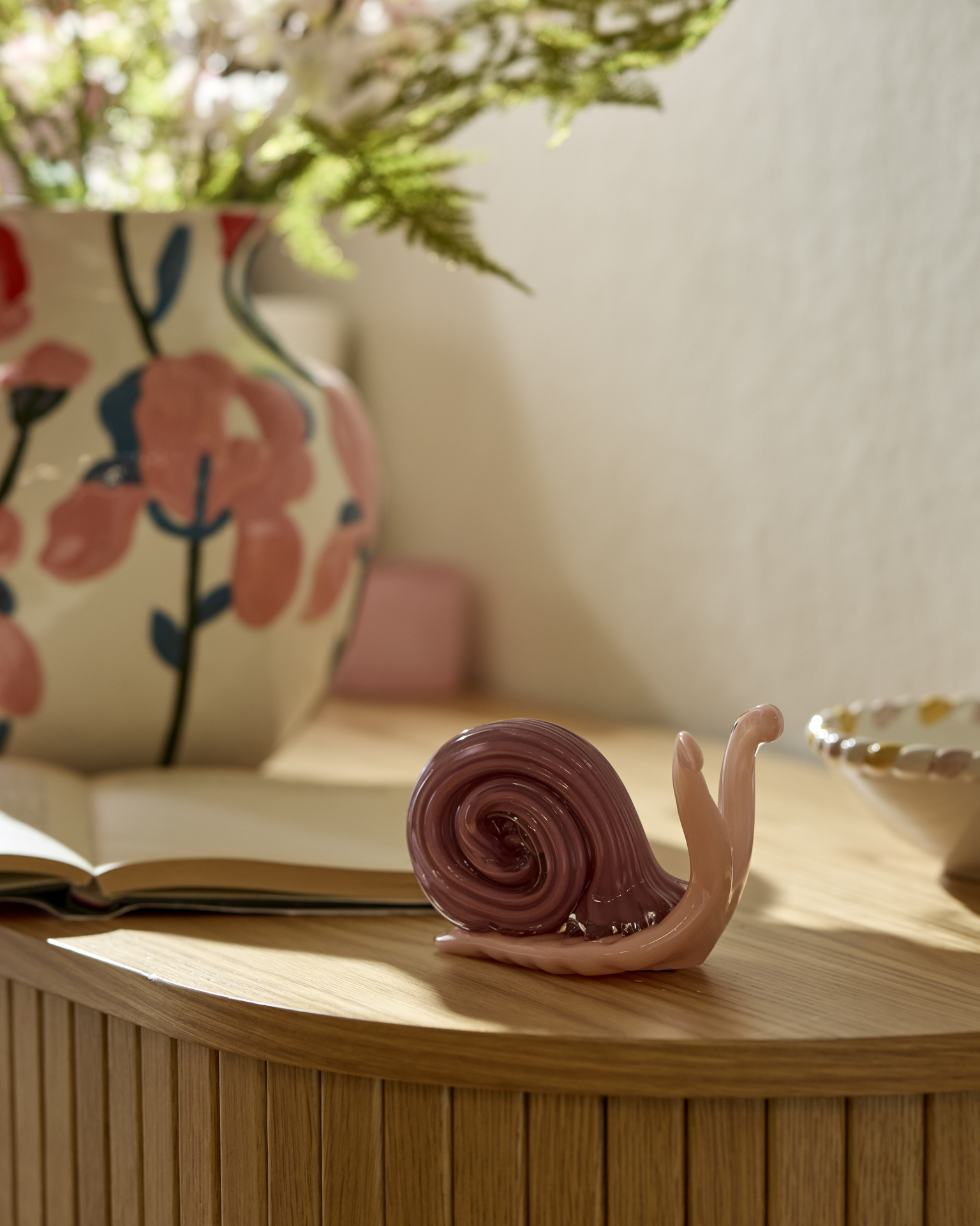 Ett prydnadsföremål i form av en rosa snigel i glas står på en skänk.