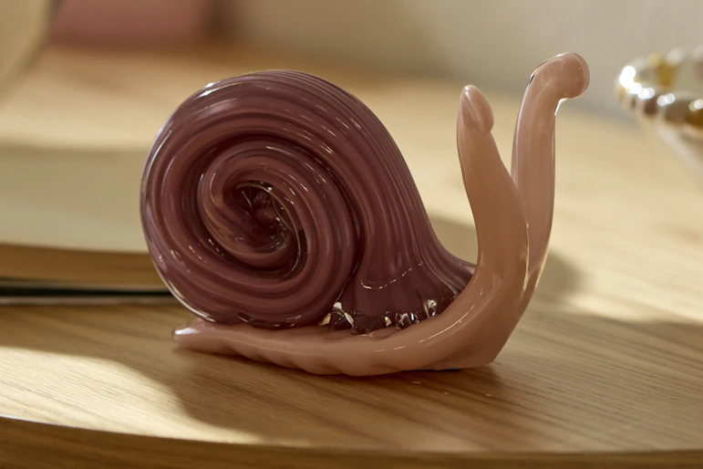 På ett sidobor i ek står en rosa snigel i glas