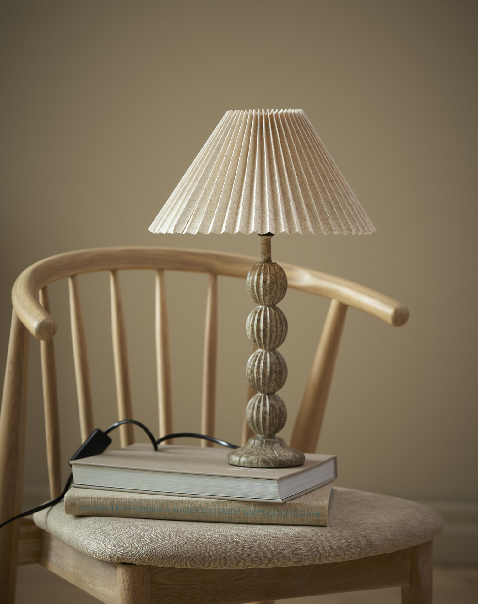 På en stol ståe en lampfot med plisserad skärm