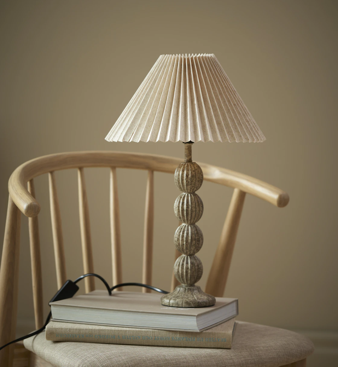 På en stol ståe en lampfot med plisserad skärm