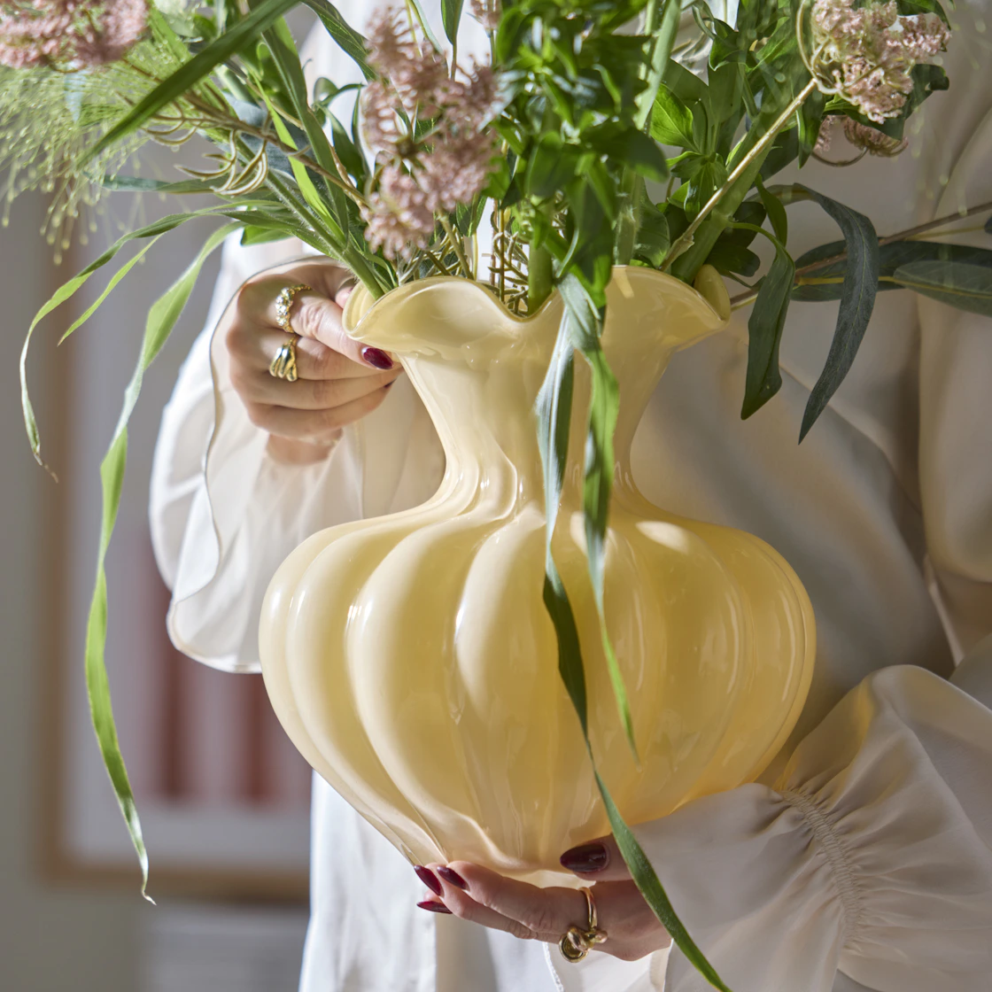 En person håller en gul glasvas med en bukett.
