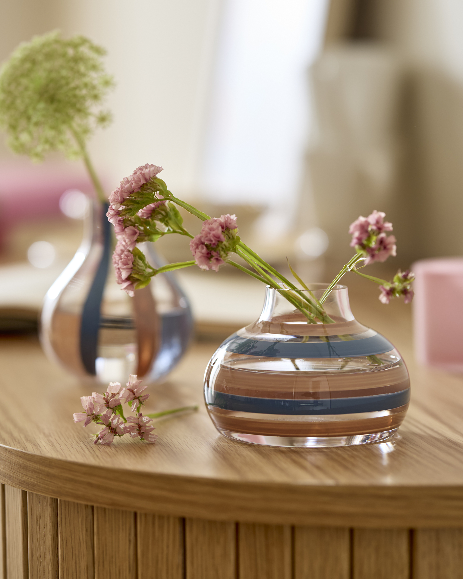 Två små randiga glasvaser i blått och rosa står på en skänk.