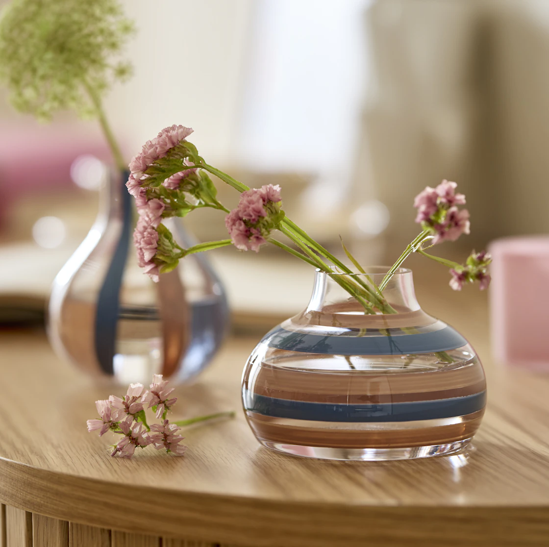 Två små randiga glasvaser i blått och rosa står på en skänk.