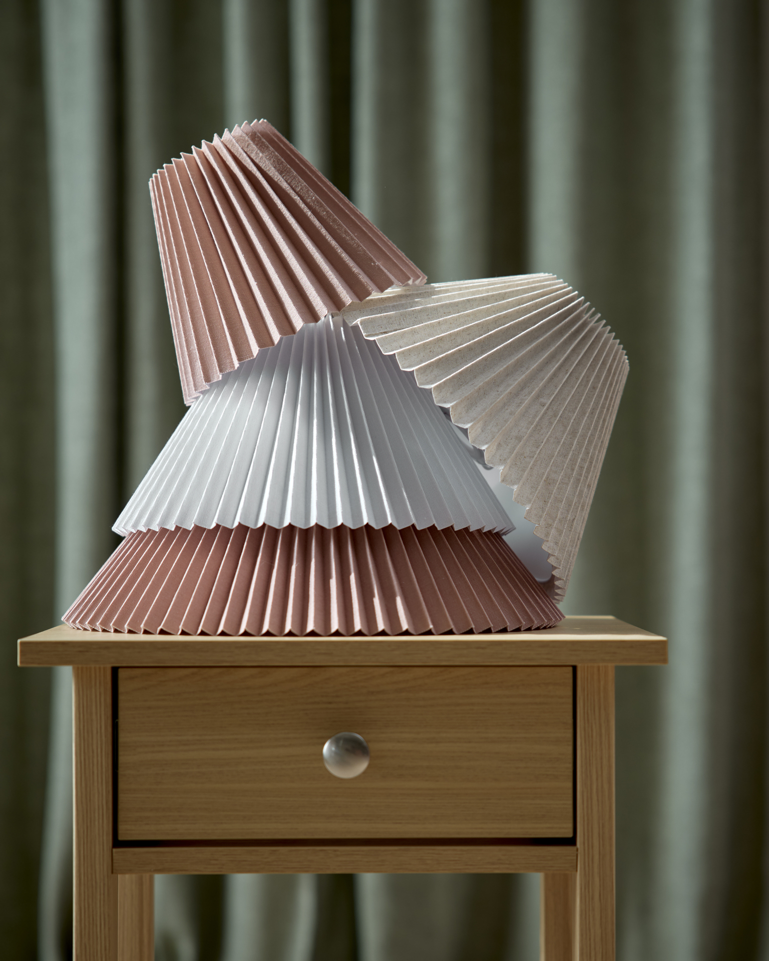 På ett sängbord är flera plisserade skärmar i olika färger och storlekar staplade