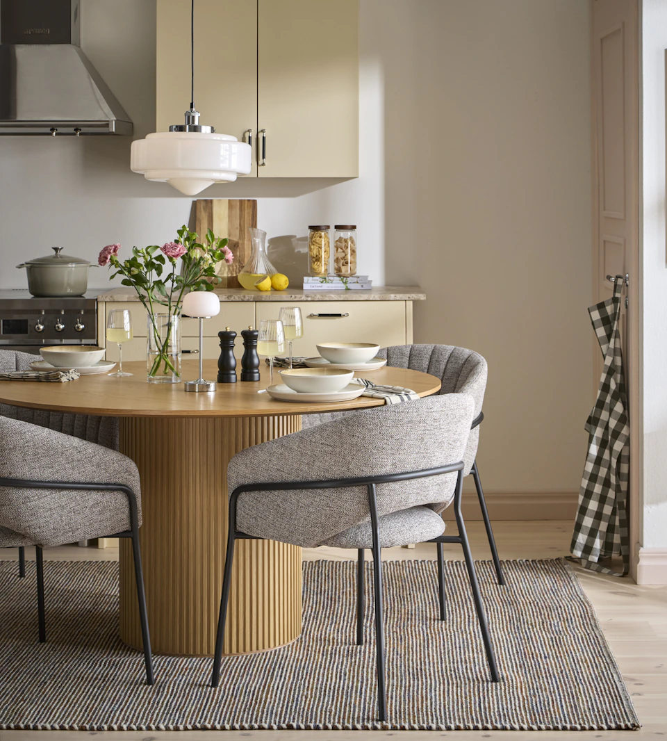Ett runt ekbord och fyra tygklädda gråa stolar står i ett ljusgult kök.