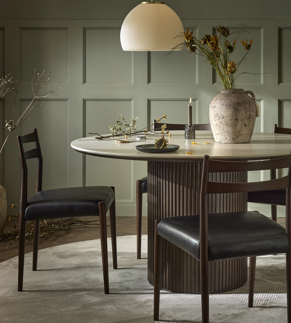 Ett runt bord och fyra stolar i mörkt trä står i ett rum med gröna väggar.