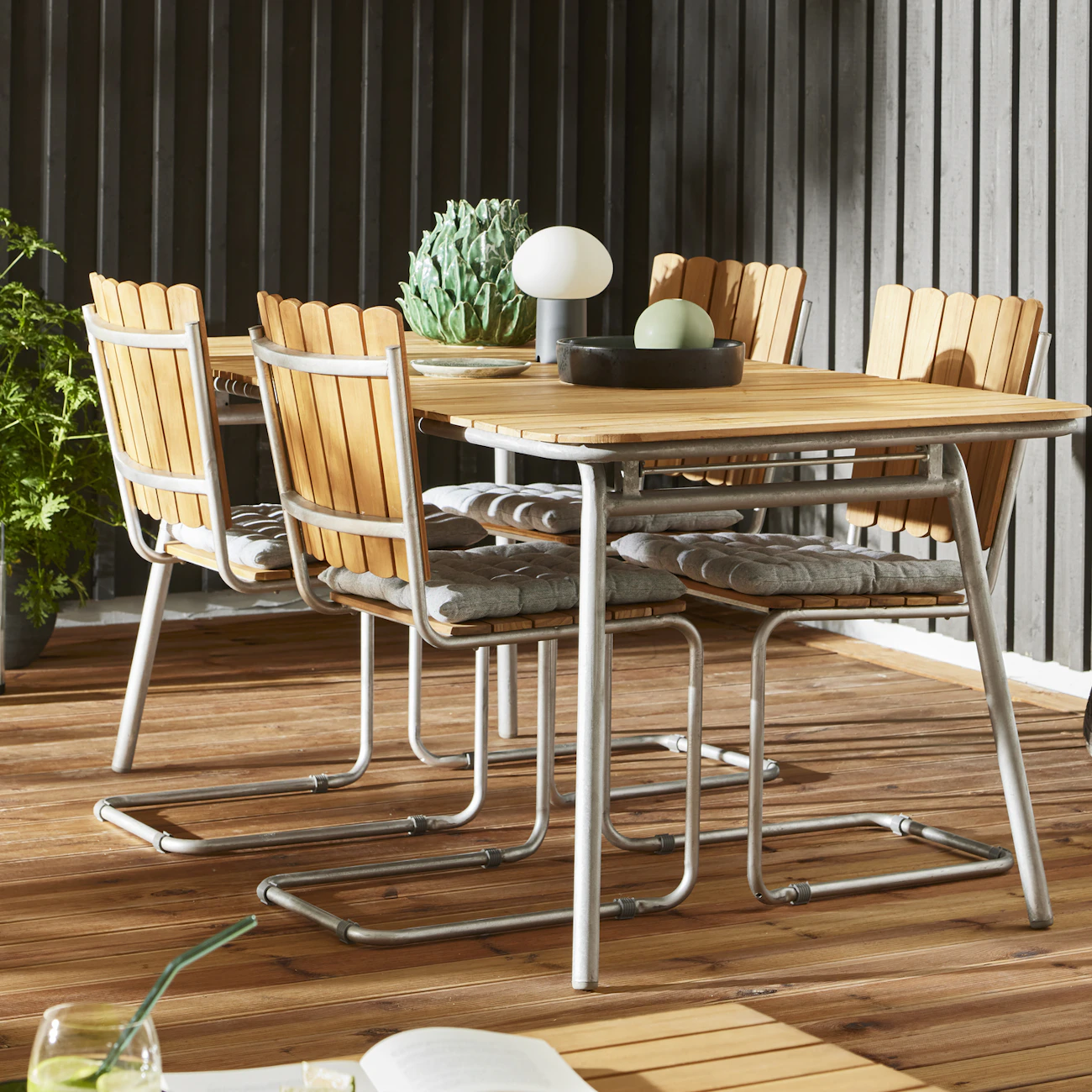 Ett rektangulärt bord och fyra stolar i teak står på ett trädäck.