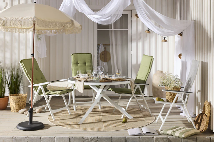 Ett runt bord med vitt underrede och fyra matchande stolar med gröna dynor står på ett trädäck.